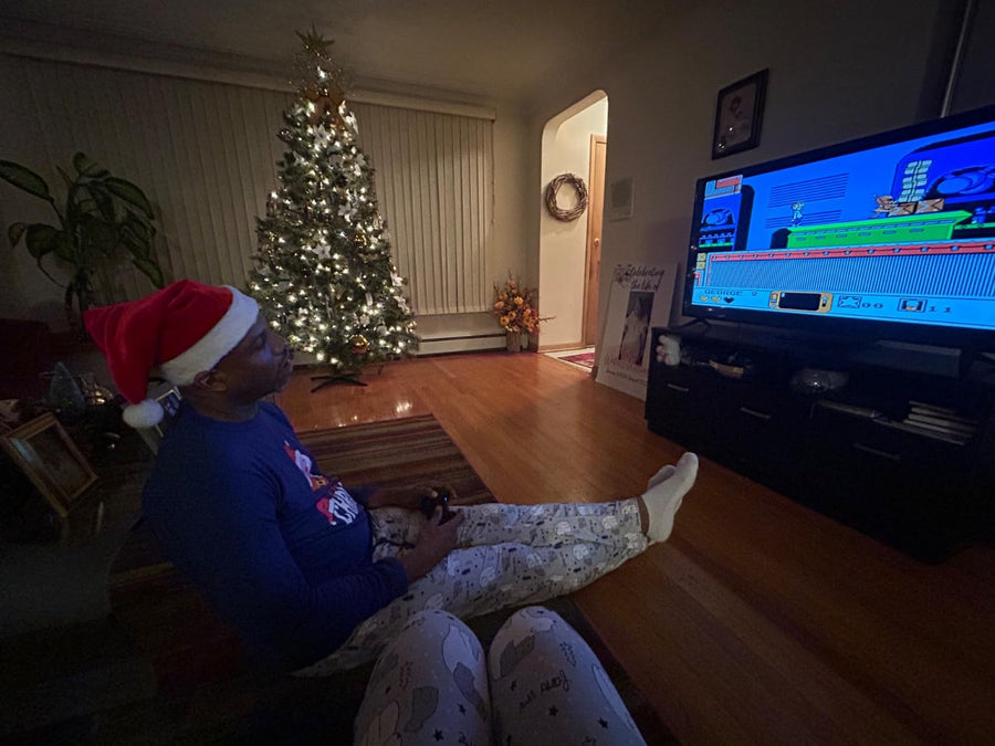 A man in a Santa hat playing a retro game beside a Christmas tree
